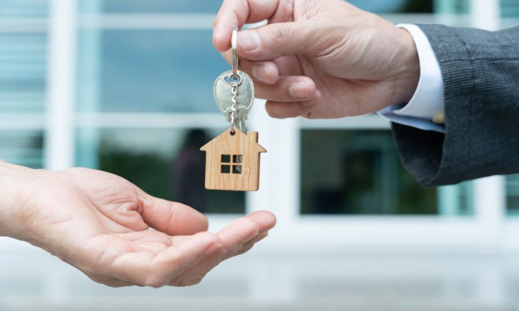 Close-up of hands exchanging a house-shaped keychain, signifying the finalization of a home purchase