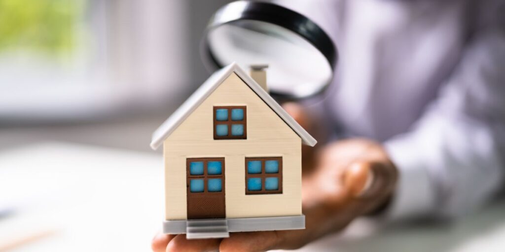 Hand holding a miniature house under a magnifying glass, symbolizing home inspection or property appraisal