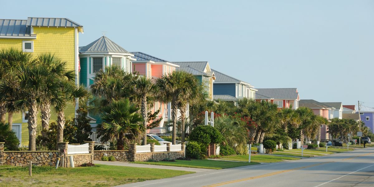 Row of colorful beachfront houses with palm trees along a street in Kure Beach.