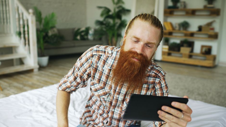 Person researches Prince Edward Island real estate on a tablet, with a bright, charming coastal home visible in the backgr...