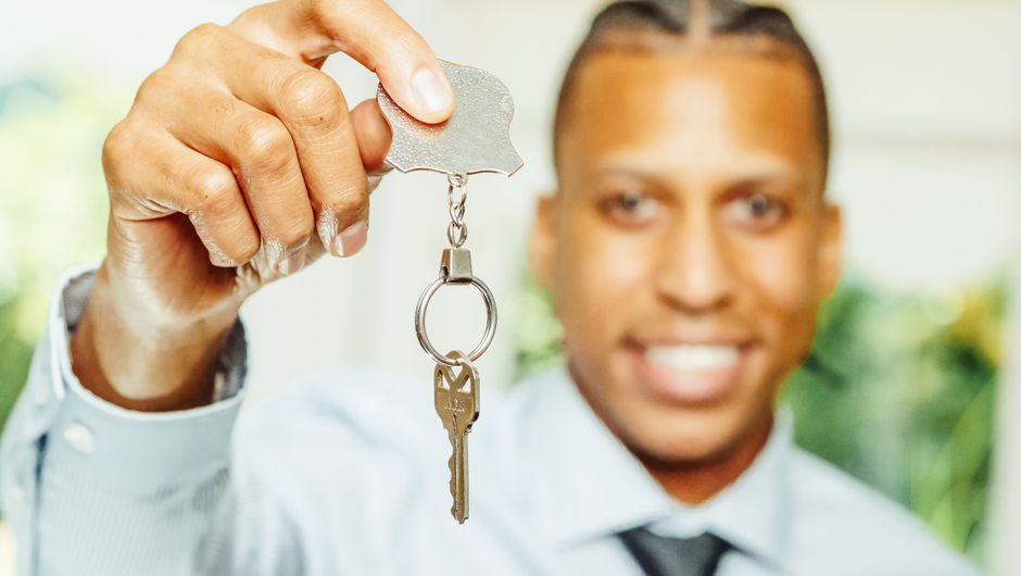 A professional and trustworthy real estate agent hands over the keys to a new home inside a bright, modern living room, representing a successful home sale.